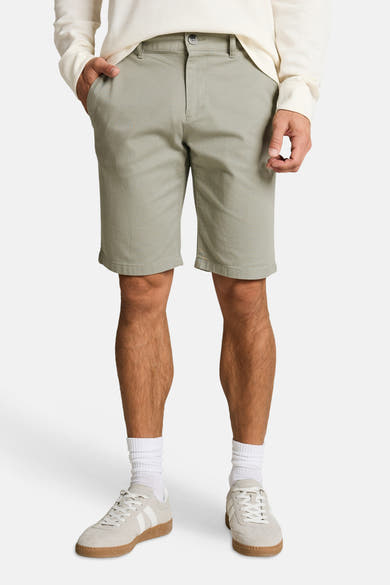 Short vert clair de Tom Tailor en coton, avec bouton et poches, porté avec un pull écru et des baskets beiges.