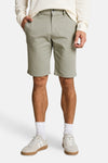 Short vert clair de Tom Tailor en coton, avec bouton et poches, porté avec un pull écru et des baskets beiges.