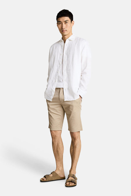 Bermuda beige de Tom Tailor, porté avec une chemise blanche ouverte sur un t-shirt et des sandales.