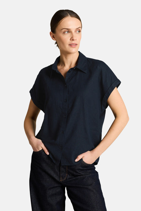 Donkerblauwe blouse met korte mouwen van Tom Tailor, klassieke kraag, gedragen met een wijde jeans, een zwarte tas en sandalen.