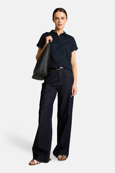 Chemisier à manches courtes bleu foncé de Tom Tailor, col classique, porté avec un jean large, un sac noir et sandales.