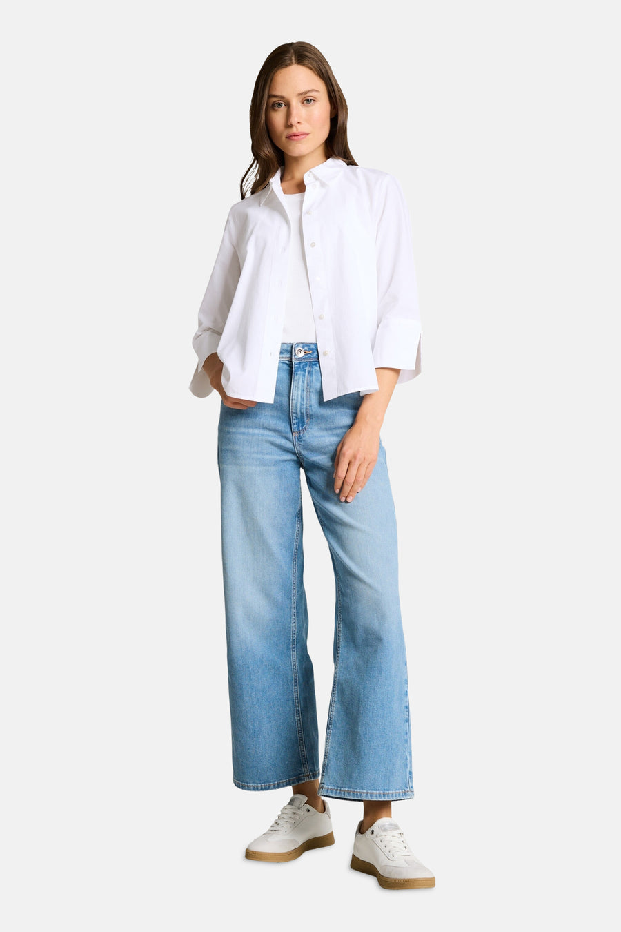 Chemise blanche à manches longues de Tom Tailor, portée ouverte sur un débardeur blanc, avec un jean large et des baskets blanches.