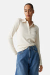 T-shirt beige à manches longues d'OPUS, en maille côtelée, porté avec un jean taille haute bleu.
