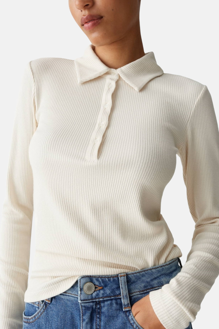 T-shirt à manches longues beige d'OPUS, en maille côtelée, porté avec un jean bleu taille haute.
