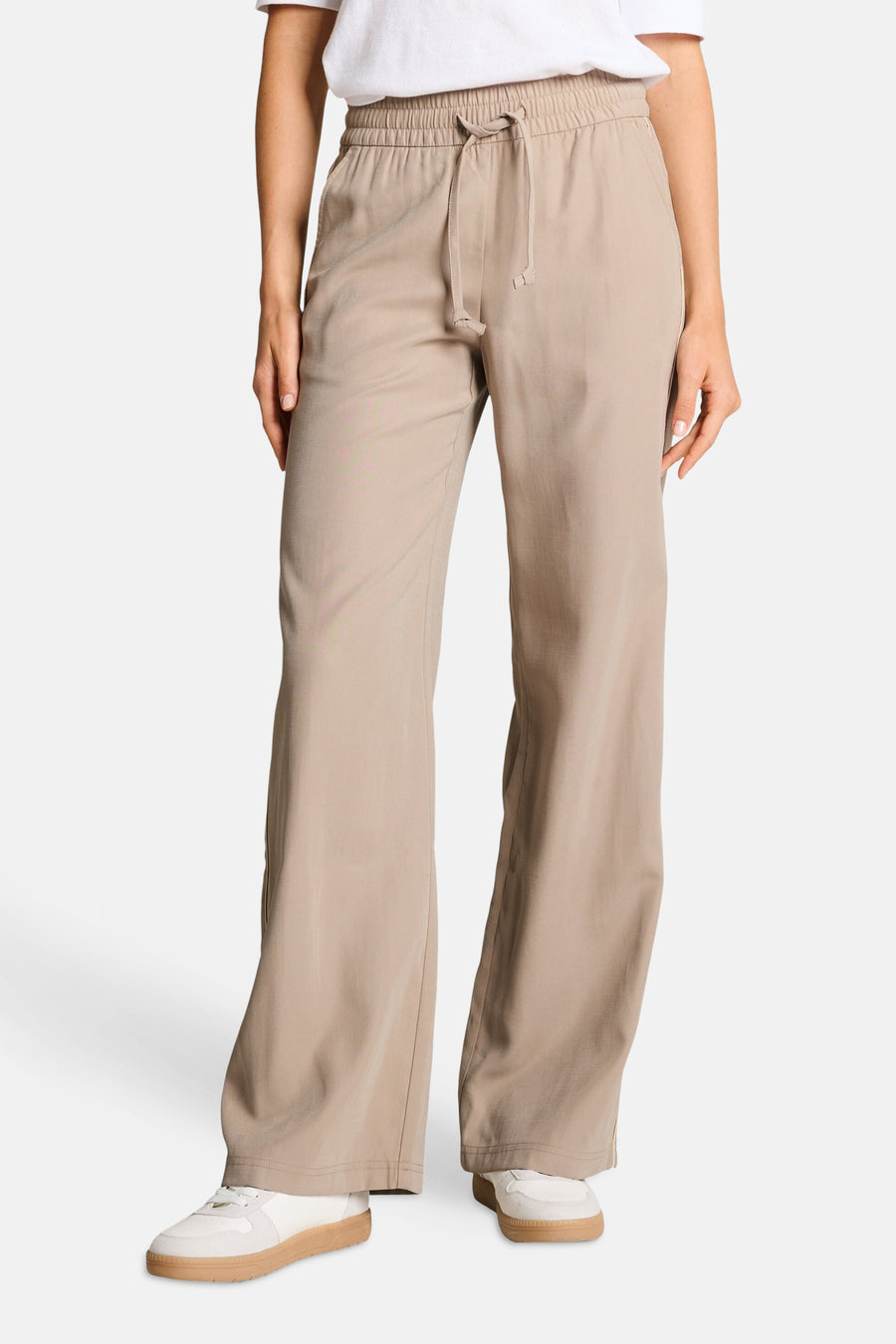 Pantalon taupe de Tom Tailor à taille élastiquée avec cordon de serrage, coupe ample, porté avec un t-shirt blanc et des baskets.