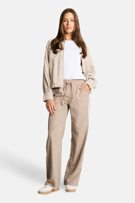Pantalon taupe de Tom Tailor, coupe décontractée avec taille élastique à cordon, porté avec un t-shirt blanc et une veste beige.