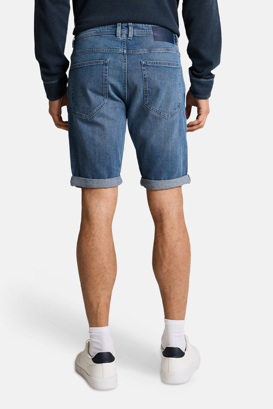 Short en jeans mid blue denim de Tom Tailor, vue de dos, ourlets retroussés, porté avec un pull foncé et des baskets blanches.
