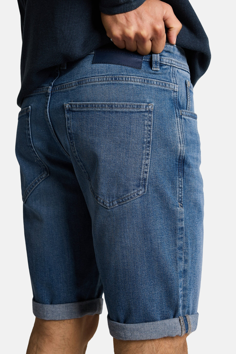 Short en jeans bleu denim moyen de Tom Tailor, vue arrière avec patch logo, ourlets roulés et un pull marine.