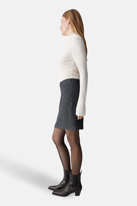 Jupe courte grise en laine d’OPUS, portée avec des collants noirs et des bottines en cuir noir, vue de profil.