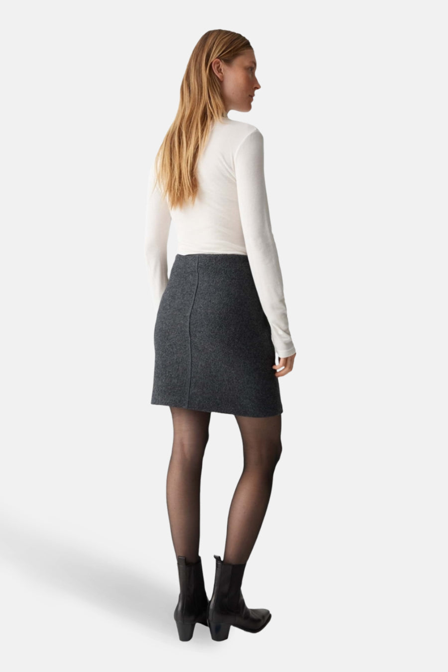 Grijze korte rok van OPUS, gedragen met een witte top met lange mouwen en een zwarte panty.