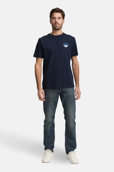T-shirt à manches courtes bleu marine de Tom Tailor, avec un imprimé discret sur la poitrine, porté avec un jean et des baskets blanches.
