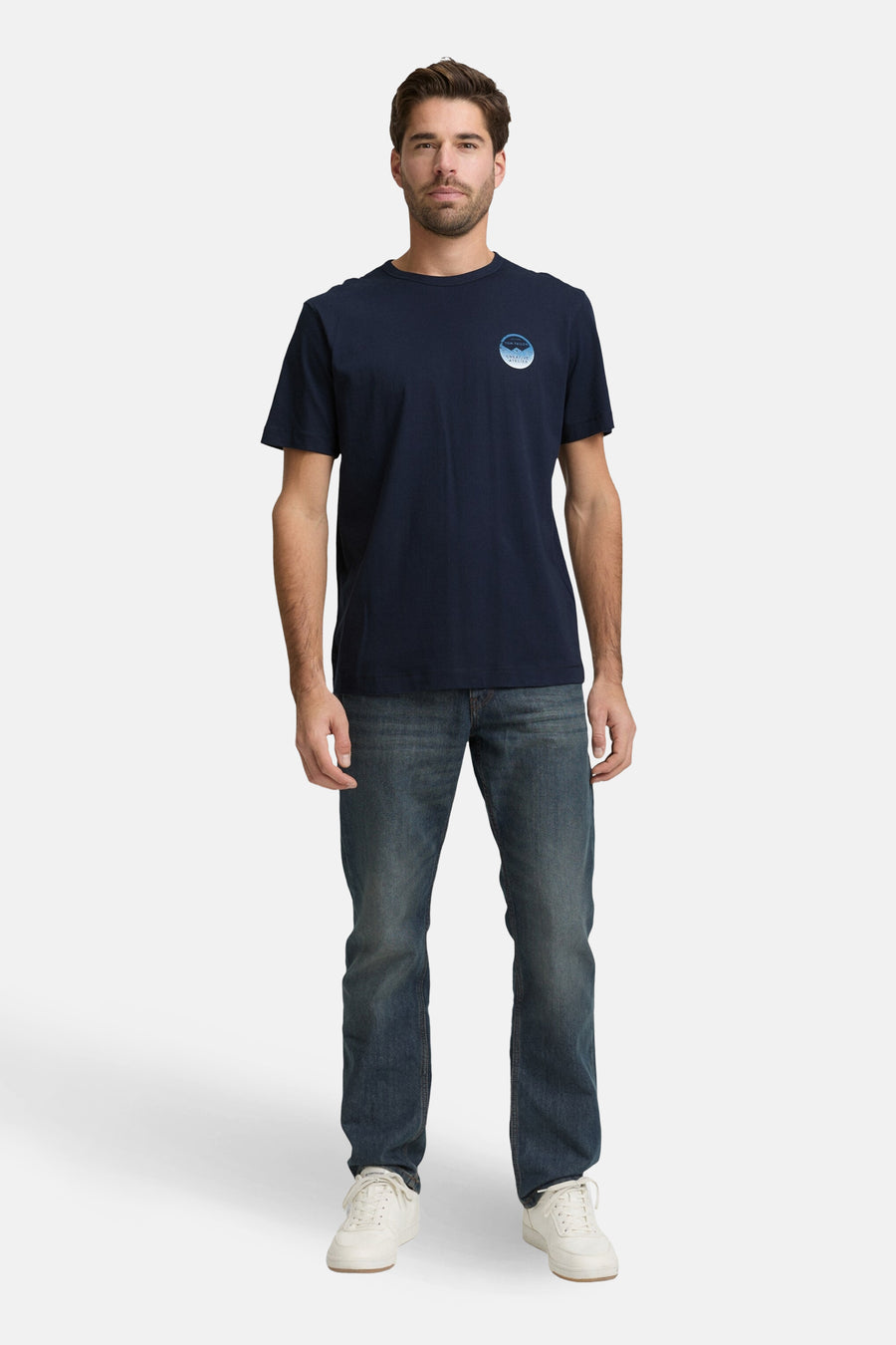 T-shirt à manches courtes bleu marine de Tom Tailor, avec un imprimé discret sur la poitrine, porté avec un jean et des baskets blanches.
