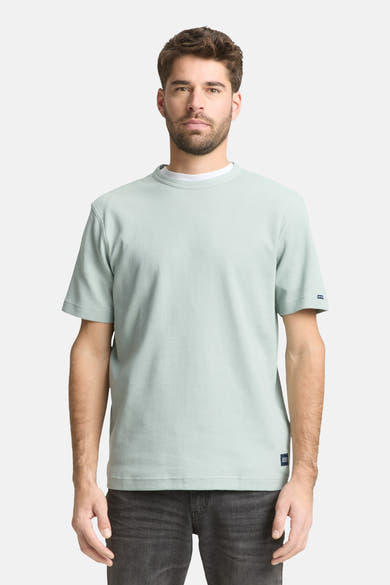T-shirt à manches courtes vert de Tom Tailor, avec texture côtelée et ourlet droit, porté avec un t-shirt blanc à col rond et un jean gris.