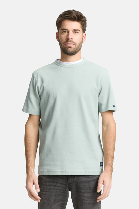 T-shirt à manches courtes vert de Tom Tailor, avec texture côtelée et ourlet droit, porté avec un t-shirt blanc à col rond et un jean gris.