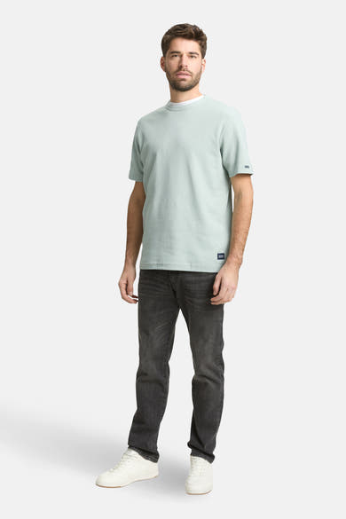 T-shirt à manches courtes vert de Tom Tailor, avec un col rond et une texture gaufrée, porté avec un jean noir et des baskets blanches.
