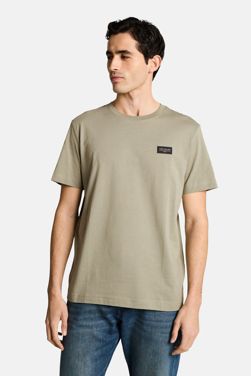T-shirt kaki de Tom Tailor, avec un logo carré sur la poitrine, porté avec un jean bleu.
