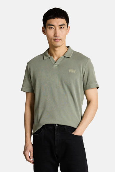 Tom Tailor poloshirt met wafelstructuur en V-hals, gedragen door een man met een zwarte jeans en witte sneakers.