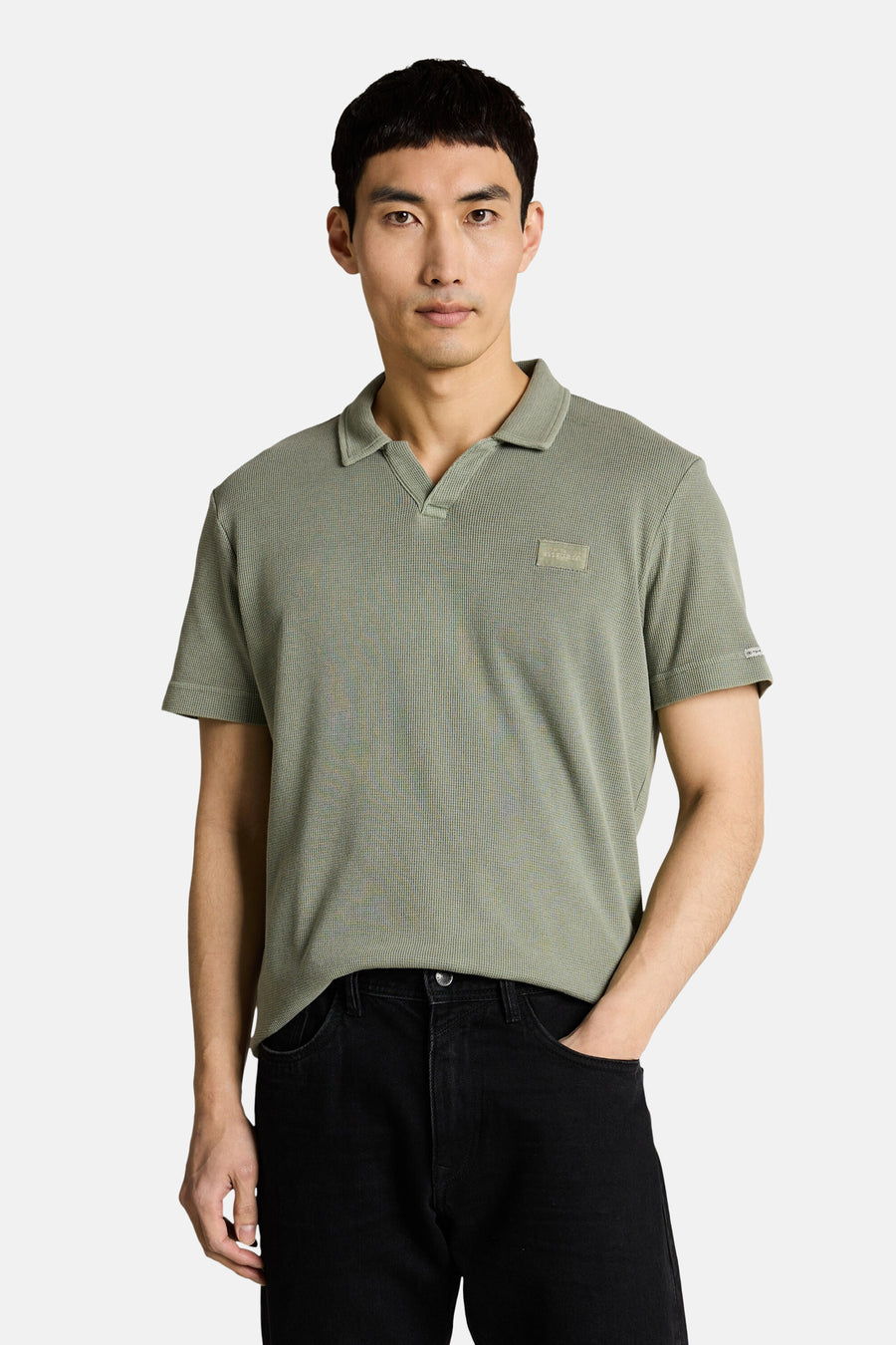 Tom Tailor poloshirt met wafelstructuur en V-hals, gedragen door een man met een zwarte jeans en witte sneakers.
