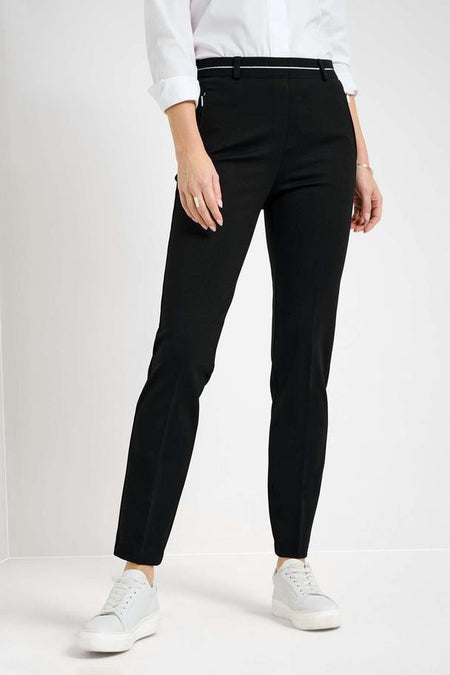 Pantalon noir de RAPHAELA avec une bande blanche à la taille, porté avec une chemise blanche et des baskets blanches.
