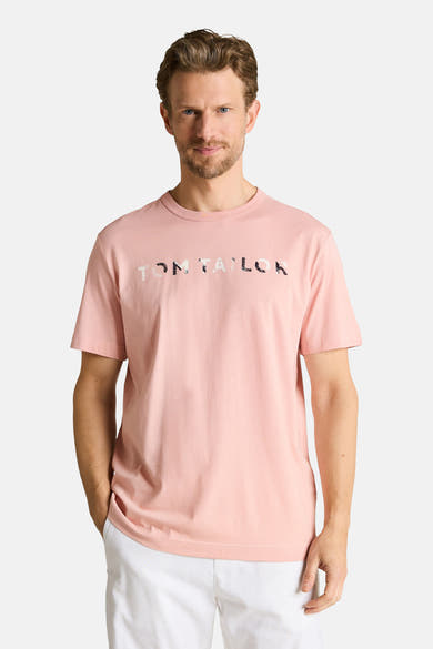 Roze T-shirt van Tom Tailor met TOM TAILOR-opschrift met patroon, gedragen door een man in een witte korte broek.