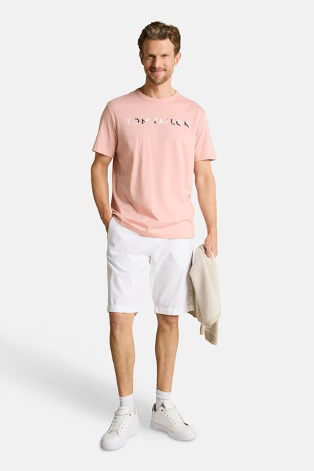 T-shirt rose de Tom Tailor avec lettrage TOM TAILOR à motifs, porté par un homme en short blanc.