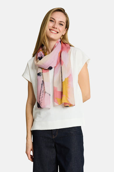 Foulard multicolore de Tom Tailor à motifs abstraits rose, jaune et noir, porté sur un top blanc texturé et un jean foncé par une femme souriante.