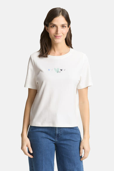 T-shirt blanc à manches courtes de Tom Tailor, orné de motifs cœurs délicats, porté avec un jean bleu.
