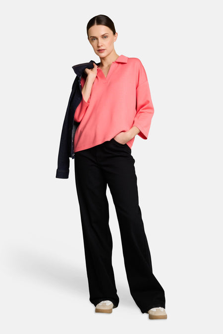 Polo corail de Tom Tailor, avec un jean bleu foncé sur l'épaule et un pantalon noir ample.
