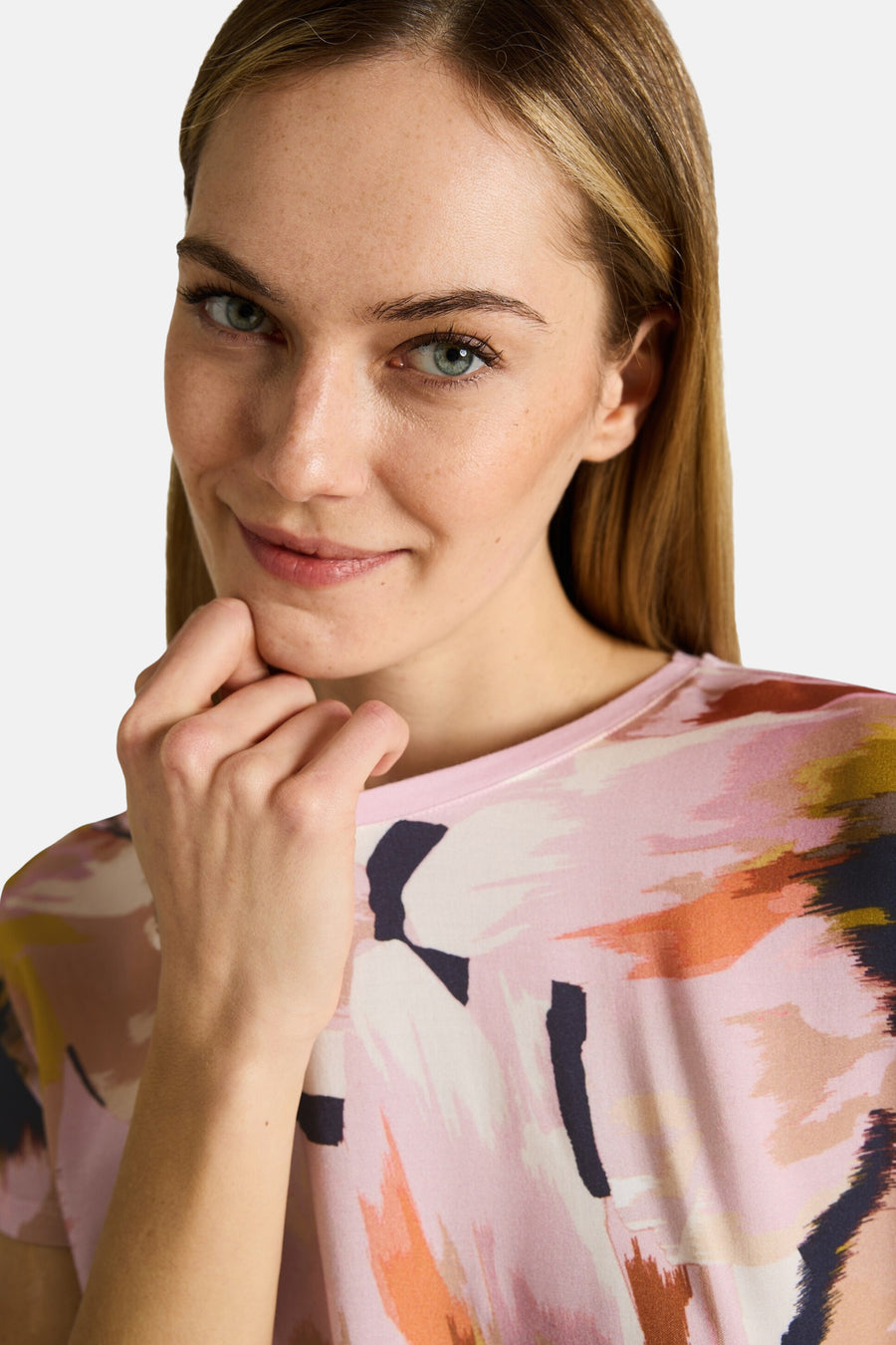 T-shirt à manches courtes multicolore de Tom Tailor avec un motif abstrait rose, orange et noir, porté par une femme souriante.