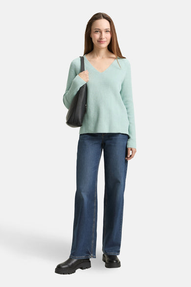 Pull à col en V vert de Tom Tailor, porté avec un jean bleu ample et un sac à main noir.