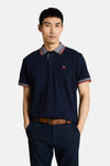 Donkerblauwe polo van Tom Tailor met ritssluiting, gedragen met een jasje, bijpassende broek, bruine riem en sandalen.