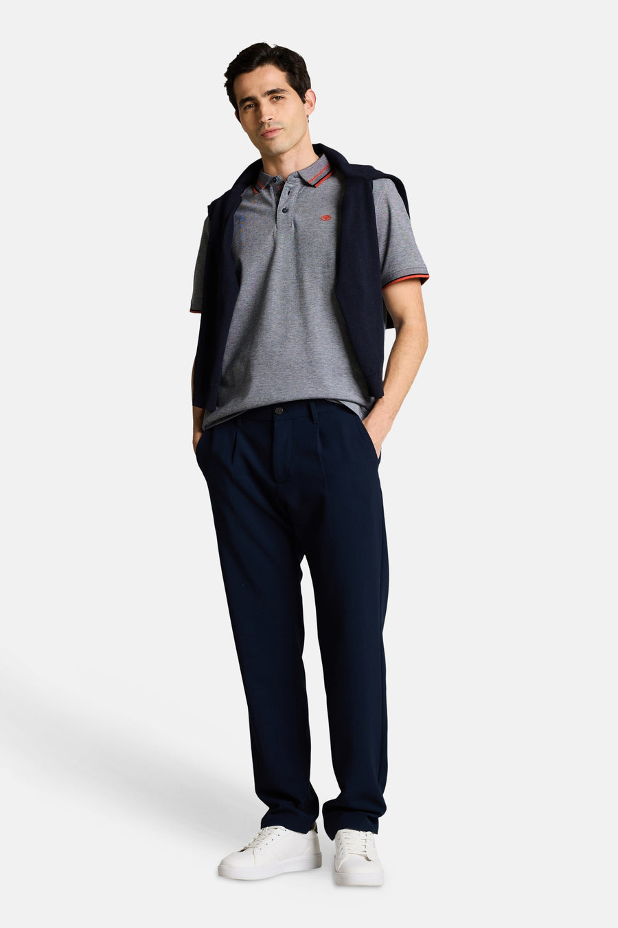 Polo gris chiné de Tom Tailor à col et manches rayés rouge et noir, avec pull marine sur les épaules, pantalon bleu marine et baskets blanches.