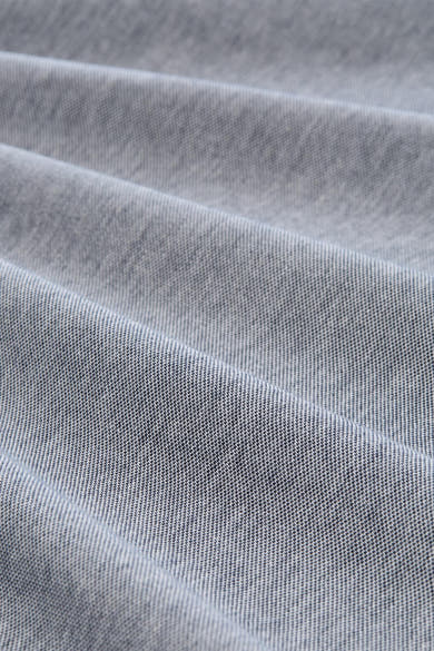 Licht grijsblauwe polo van Tom Tailor, close-up van de pique geweven stof en zachte plooien.