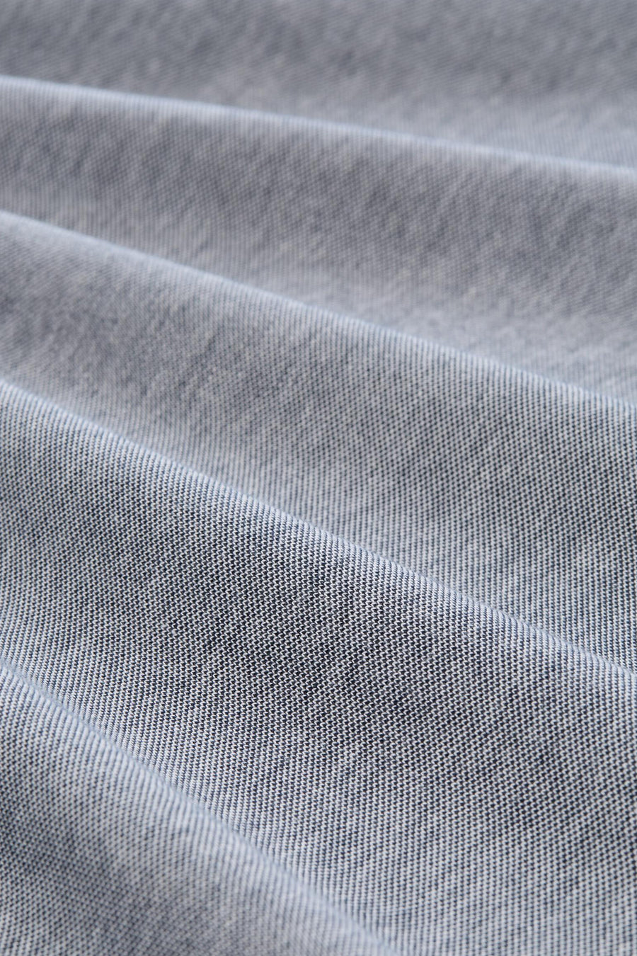 Licht grijsblauwe polo van Tom Tailor, close-up van de pique geweven stof en zachte plooien.