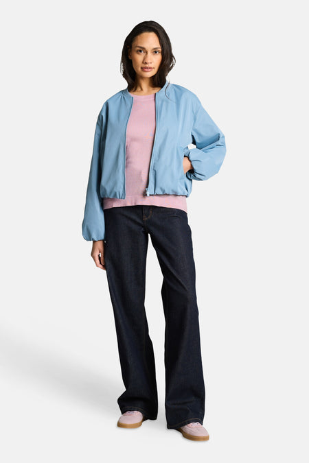Pull col rond rose de Tom Tailor, porté avec une veste bomber bleue, un jean ample bleu foncé et des baskets roses.