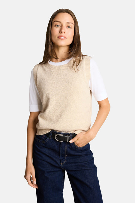 Beige mouwloze top van Tom Tailor, gedragen over een wit T-shirt met een donkerblauwe high-waist jeans en een zwarte riem.