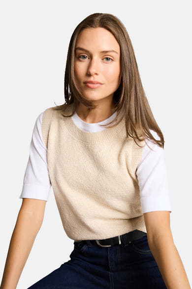 Beige mouwloos topje van Tom Tailor gedragen over een wit T-shirt en een donkerblauwe jeans met een zwarte riem.