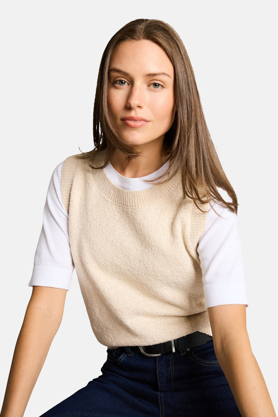 Beige mouwloos topje van Tom Tailor gedragen over een wit T-shirt en een donkerblauwe jeans met een zwarte riem.