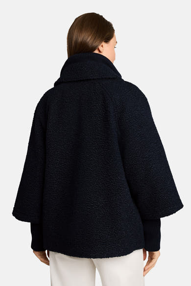 Navy blue textured poncho with ribbed collar and wide sleeves, back view, worn with white pants