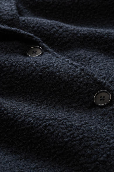 Blue textured poncho with dark buttons, close-up view showing fabric detail and stitching
