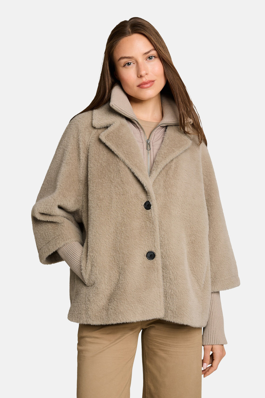 Taupe faux fur poncho with wide collar and black buttons, worn over ribbed sweater and beige pants, front view