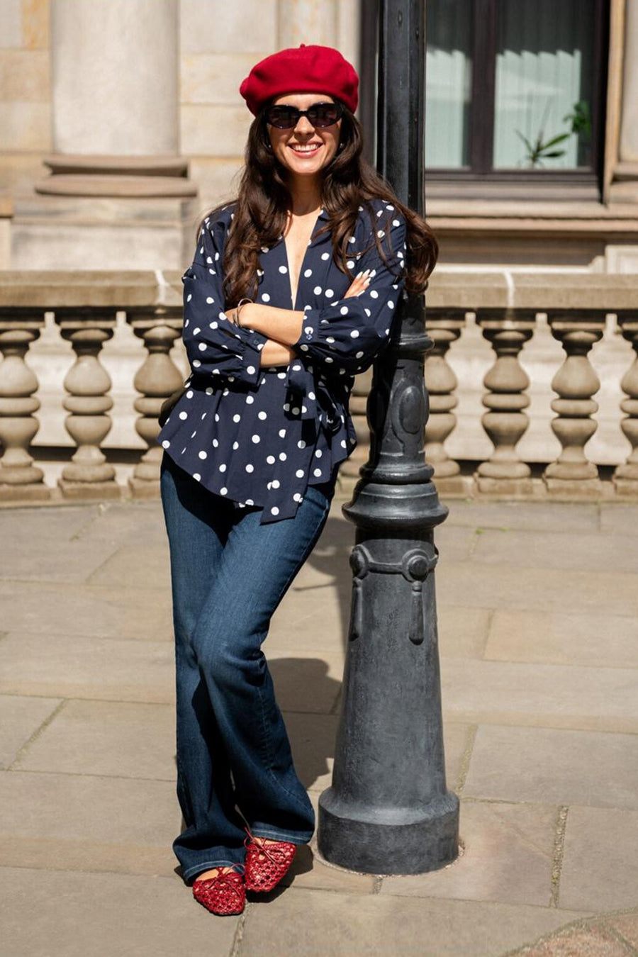 Navy blue short-sleeve blouse with white polka dots by Tom Tailor, worn with flared jeans and red beret, full-body lifestyle view