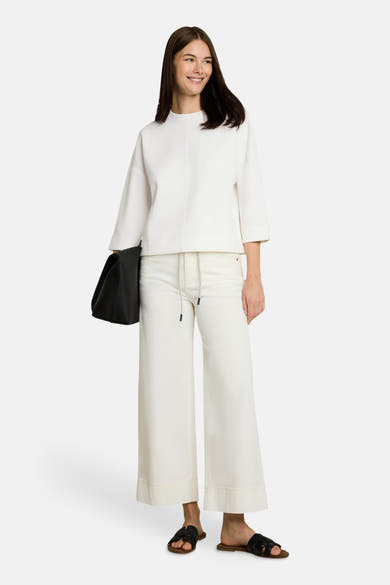 White crewneck sweatshirt with relaxed fit and three-quarter sleeves, worn with cream wide-leg pants and black sandals, full-length front view.