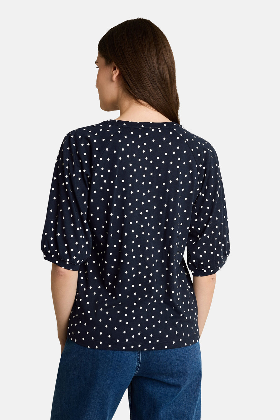 Navy blue blouse with white polka dots and 3/4 sleeves, back view, worn with blue jeans