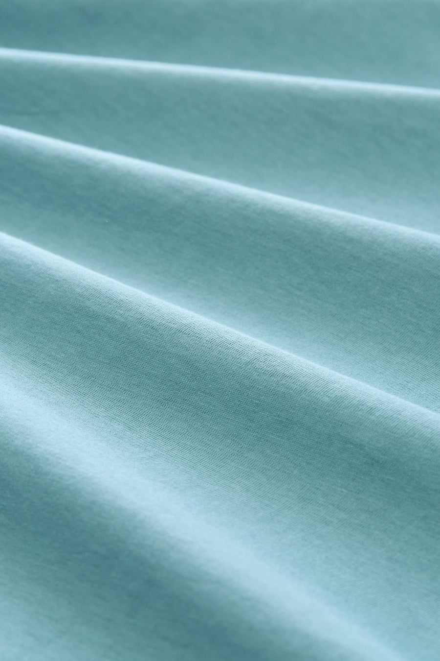 Blue short-sleeve t-shirt fabric close-up, soft textured knit with gentle folds and smooth finish.