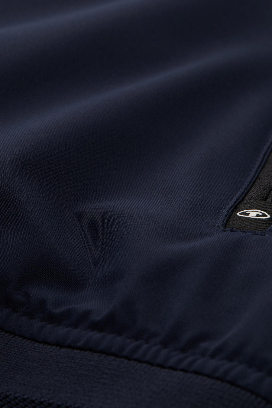 Korte blauwe jas van Tom Tailor, met gladde textuur en subtiel embleem, naaddetail onderaan.