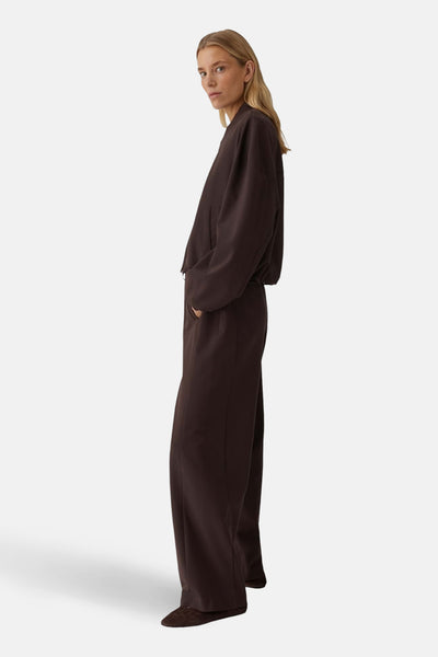 Veste courte brune par OPUS, avec manches longues et poches latérales, portée avec un pantalon assorti.