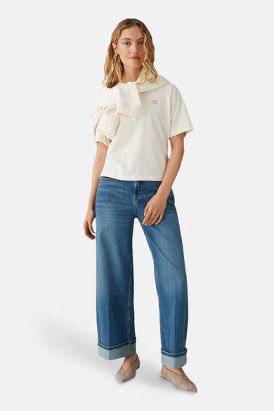 Top uni manches courtes beige d'OPUS, orné d'un cœur rouge, porté avec un foulard blanc et un jean taille haute.
