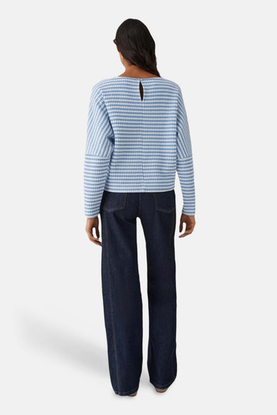 Pull col rond bleu de OPUS, à rayures horizontales, porté avec un pantalon large bleu marine.
