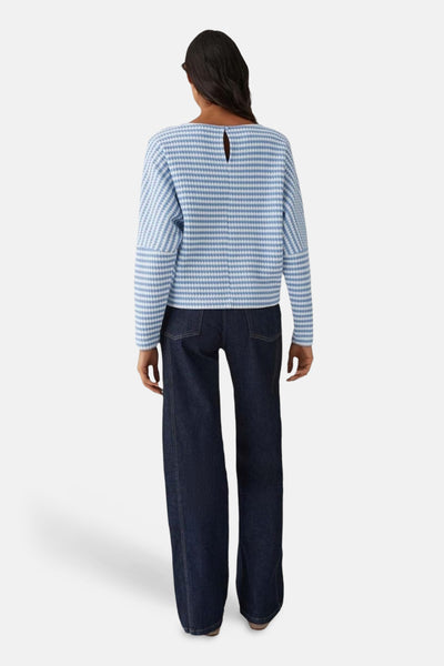 Pull col rond bleu de OPUS, à rayures horizontales, porté avec un pantalon large bleu marine.
